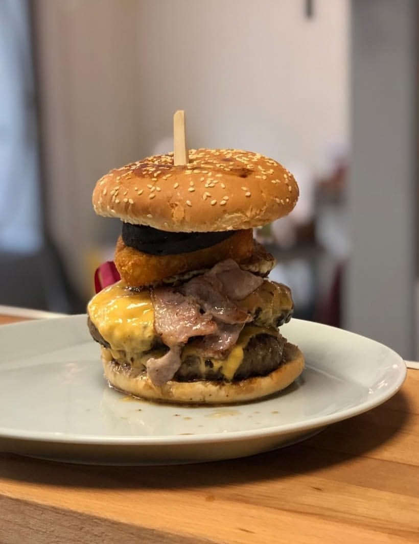 A tall burger on a white plate, photographed by Castle View Cafe in February 2019.